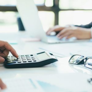 hand using calculator with glasses on table